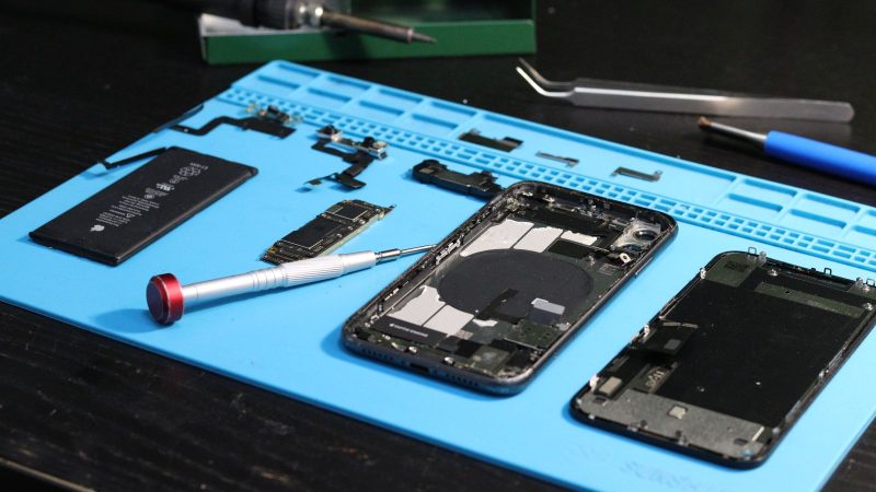 Disassembled smartphones and tools on a blue repair mat