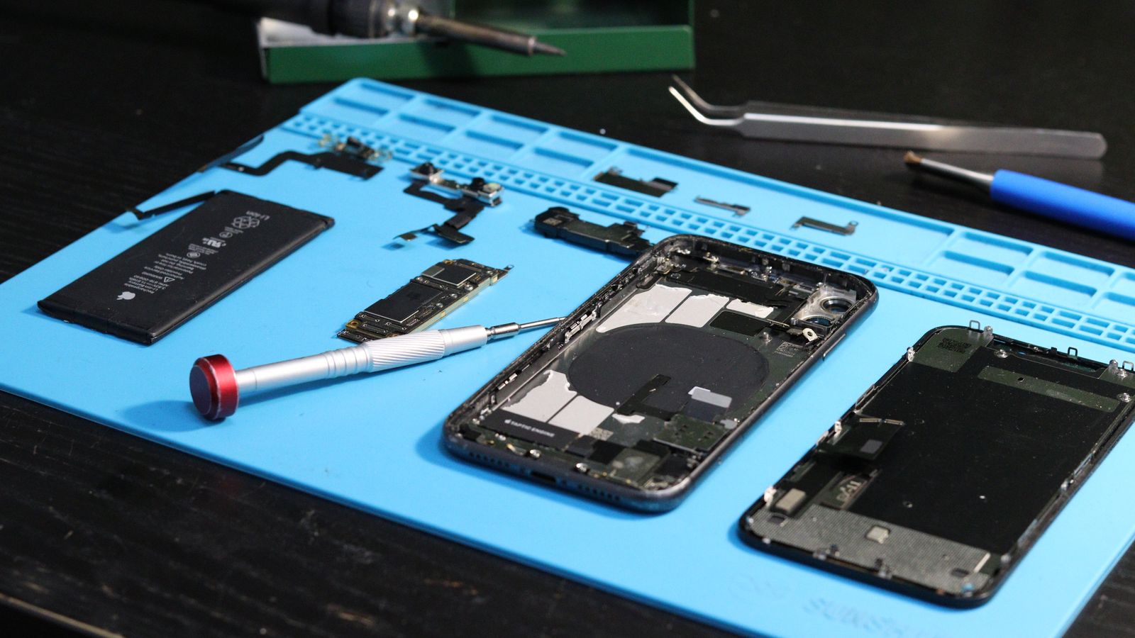 Disassembled smartphones and tools on a blue repair mat