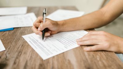 Hand filling in a paper form with a pen