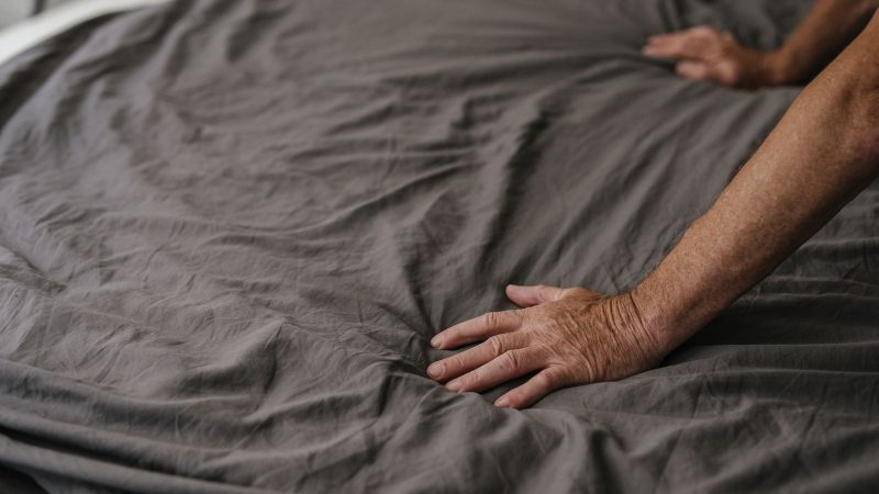 Hand pressing down on gray bed linen