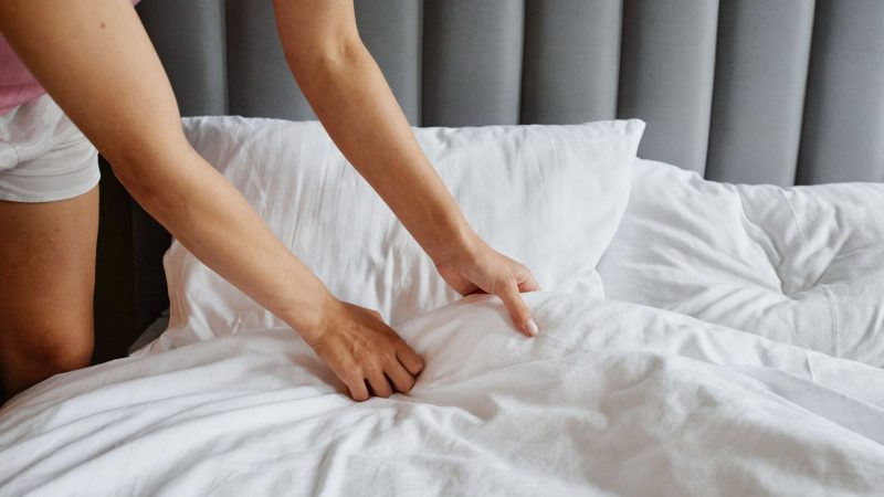 Hands smoothing a white sheet while making a bed