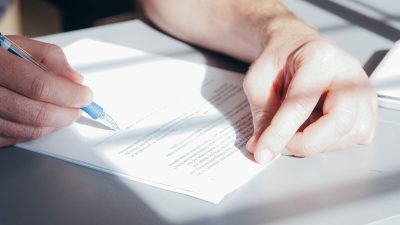 Hands signing a document with a blue pen
