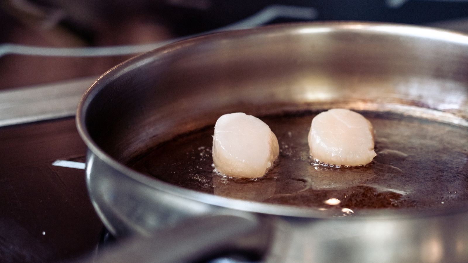 Scallops searing in a stainless steel pan
