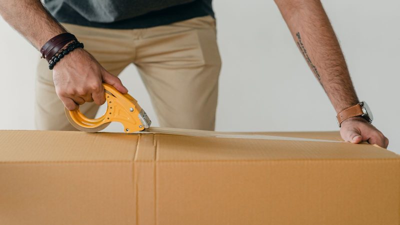 Person sealing a cardboard box with packing tape