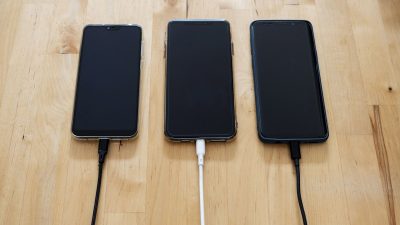 Three smartphones charging side by side on a wooden table
