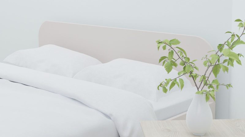 Bed with white linen beside a vase of greenery