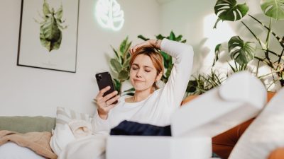 Woman frowning at her phone on a sofa beside an opened parcel